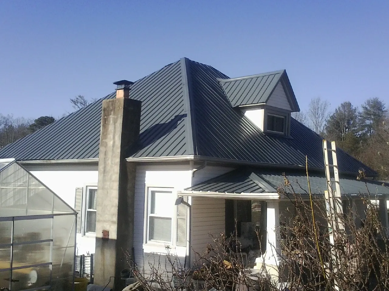 Dark blue standing seam metal roof on a white farmhouse with dormer — Slate & Tile Roof Repair by Roofing Brothers in Osterburg