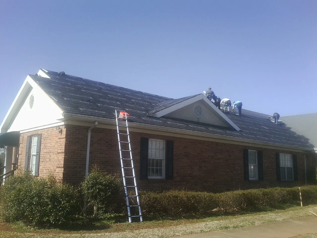 Crew tearing shingles off a brick ranch roof with a ladder set — Emergency Roof Repair work by our crew in Osterburg
