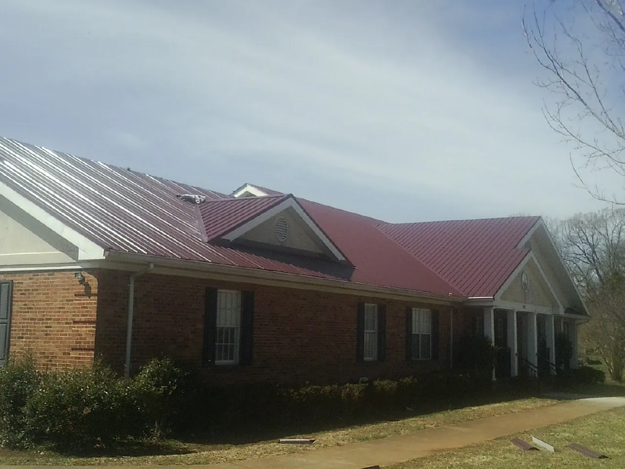 Red metal roof with gabled entries on a long brick building, from a Hail Damage Roof Repair job in Osterburg