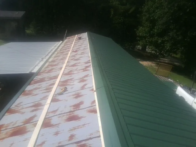 Old rusted panels beside newly installed green metal roofing — Wind Damage Roof Repair by Roofing Brothers in Osterburg
