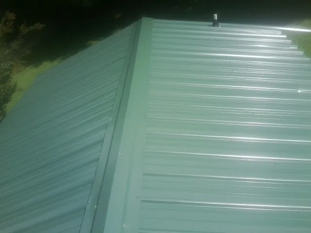New green metal panels meeting at the ridge of a roof — Flat Roof Repair work by our crew in Osterburg