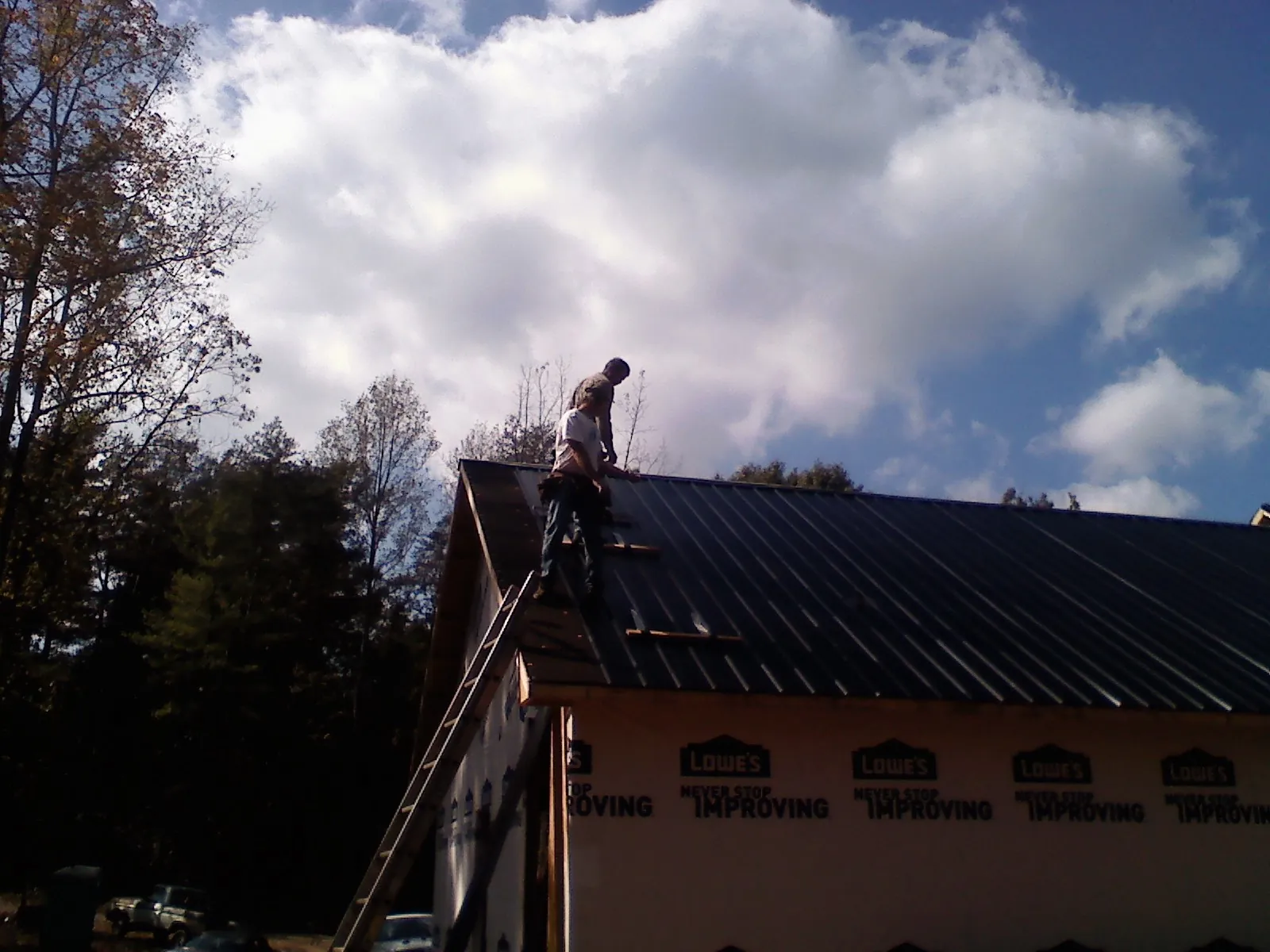 Roofer fastening dark metal panels high against a cloudy sky, from a Roof Inspection job in Osterburg