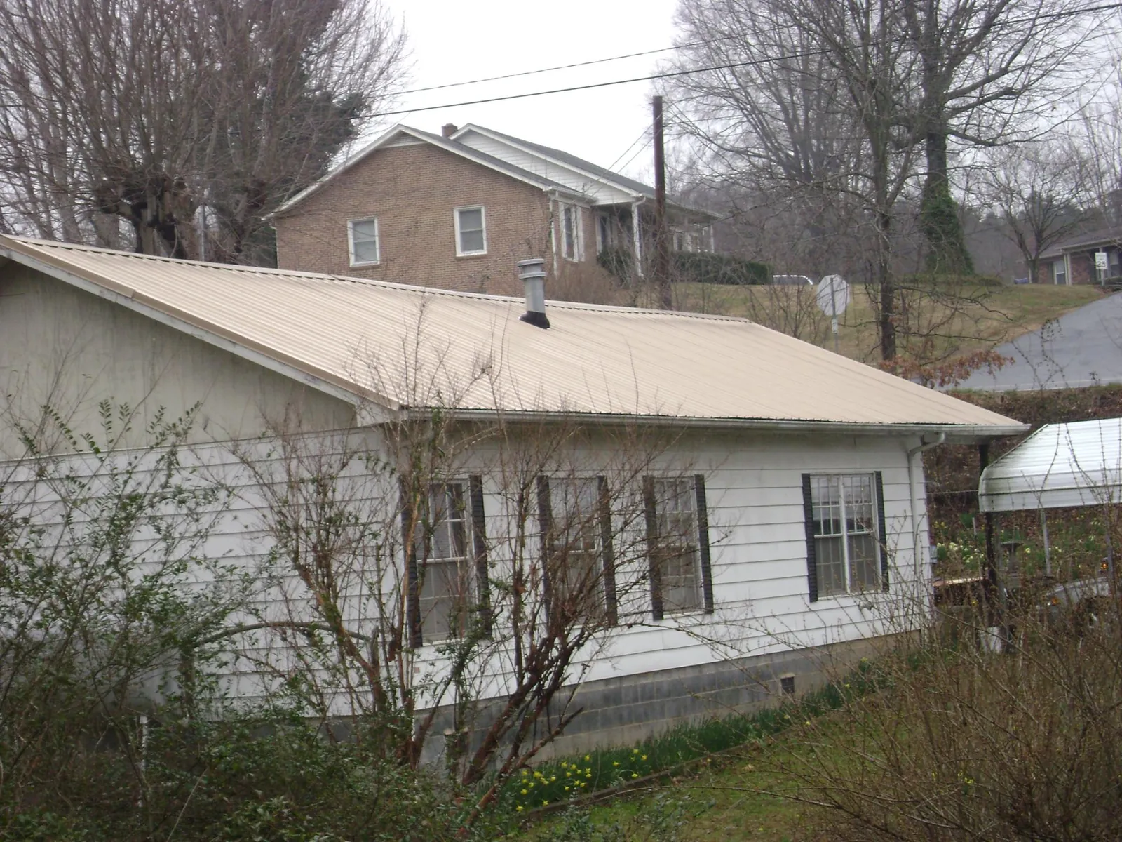 Tan metal roof on a white sided house set into a hillside — Commercial Roofing by Roofing Brothers in Osterburg