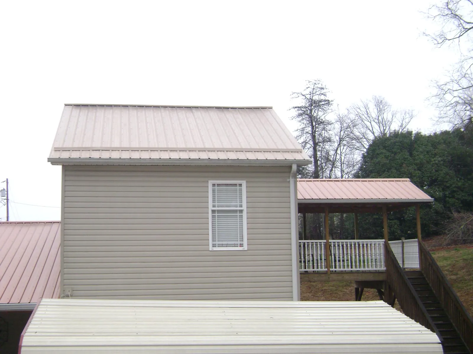 Tan metal roofs on a two story addition and attached porch, from a Roof Replacement job in Osterburg